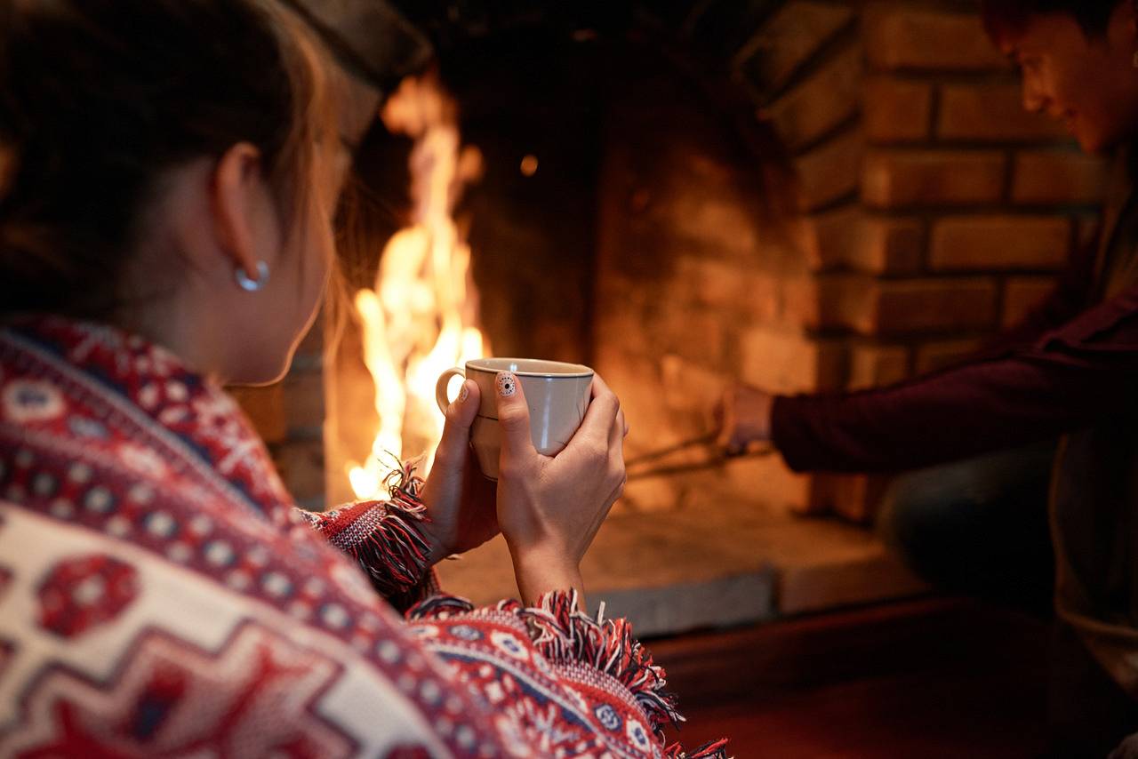 shoulder-shot-woman-warming-her-hands-mug-hot-tea-sitting-fireplace-her-boyfriend-dealing-with-charcoal_Easy-Resize.com.jpg